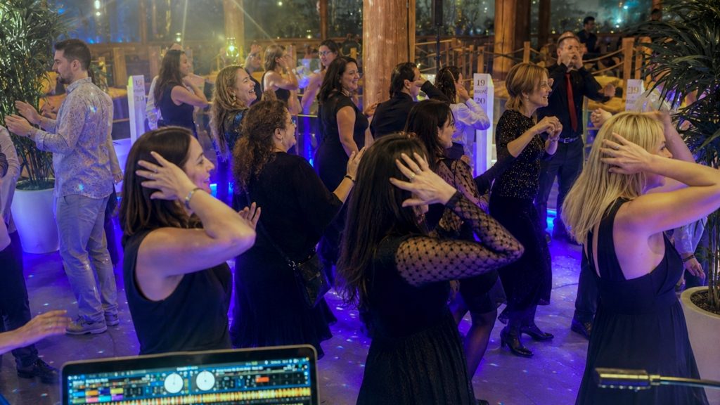 Gäste tanzen ausgelassen zu "Macarena" bei einer Firmenfeier mit blau-violetter Beleuchtung und DJ-Musik von Best Time DJs in München.