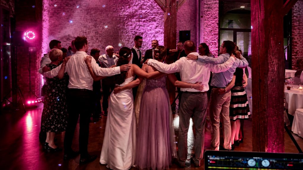 Hochzeit im Fürstenfelder Klosterhof in Fürstenfeldbruck: Das Brautpaar und seine Gäste feiern gemeinsam im festlich beleuchteten Gewölbe mit stimmungsvoller pinkfarbener Ambientebeleuchtung. Best Time DJs sorgen für musikalische Begleitung und eine ausgelassene Atmosphäre.