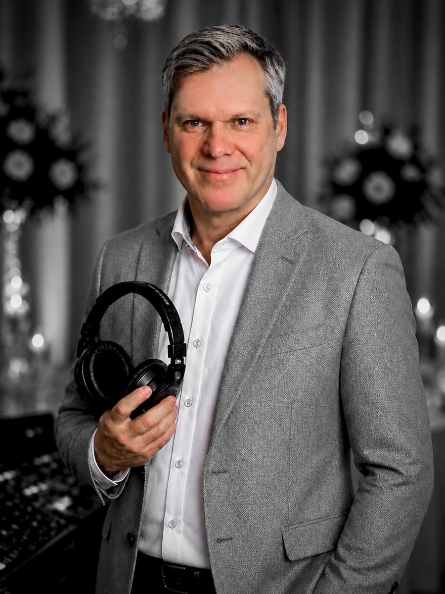 DJ Andreas von Best Time DJs aus München im grauen Sakko mit professionellen DJ-Kopfhörern vor einem DJ-Mischpult.