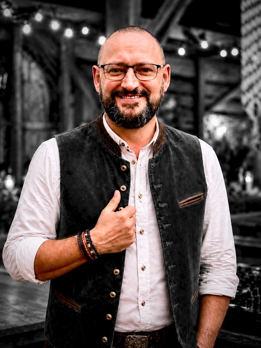DJ Peter von Best Time DJs in München mit weißem Hemd und dunkler Trachtenweste vor einer stimmungsvoll beleuchteten Eventlocation.