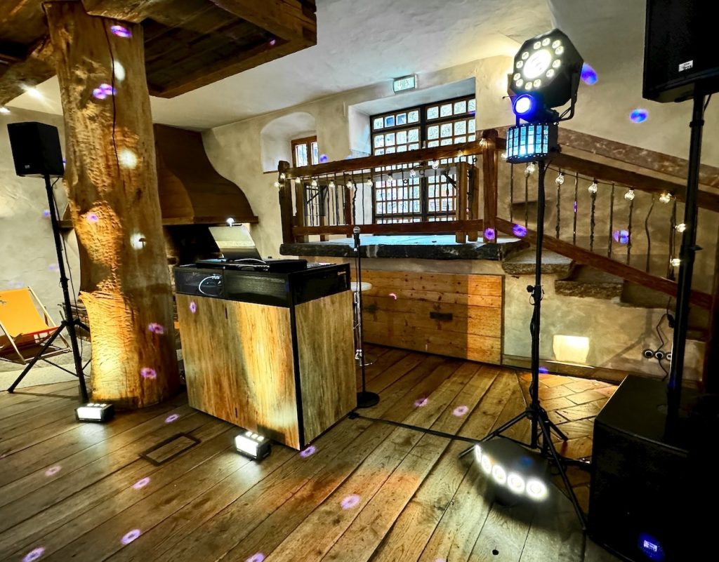 DJ-Aufbau mit Holzverkleidung, Lautsprechern und farbiger Lichteffektbeleuchtung in einer rustikalen Eventlocation.